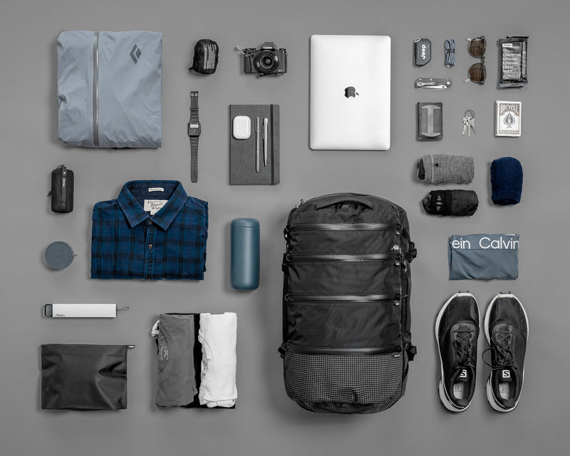 SEG28 laid flat on gray background with contents like clothing, laptop, sunglasses, snacks, and toiletries