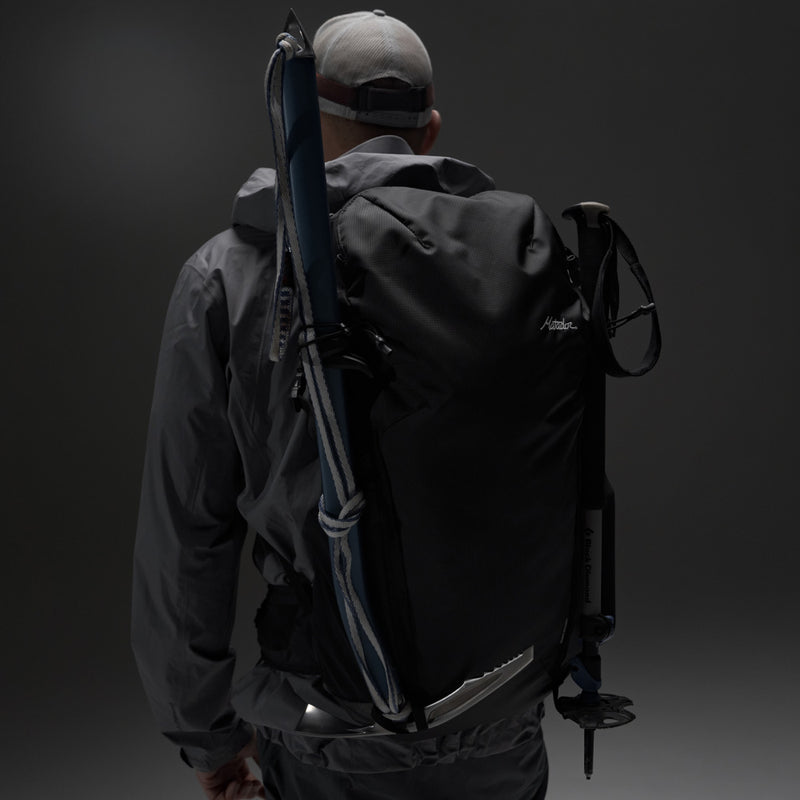 Back view of man on gray background wearing Beast28 with trekking poles and ice axe attached