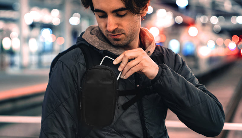 Man in city, placing cell phone in his speed stash attached to his backpack strap