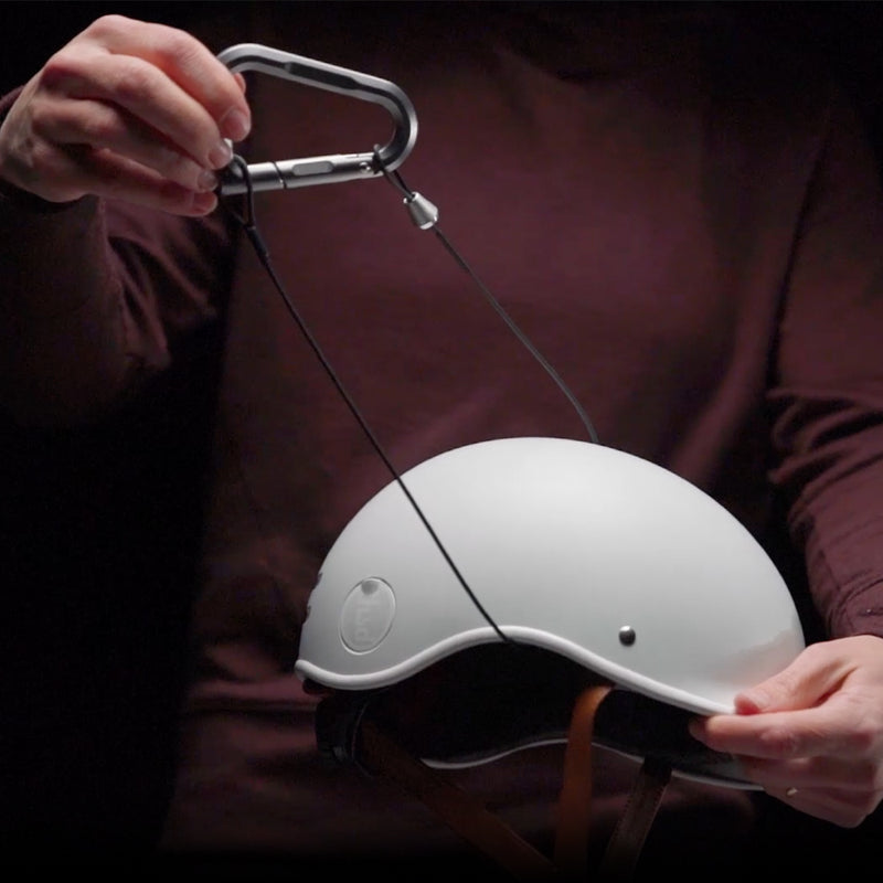 Person holding a BetaLock Accessory Cable placed through a white bike helmet