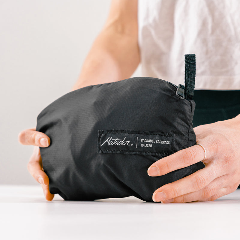 hands holding black, packed up backpack on white table