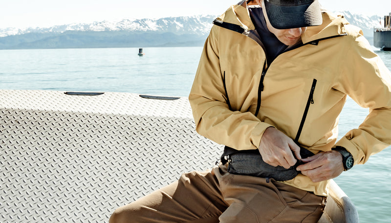 Man in yellow jacket, adjusting hip pack as he sits on a boat