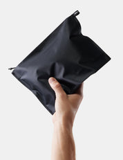 Hand holding a black zippered pouch against a light gray background