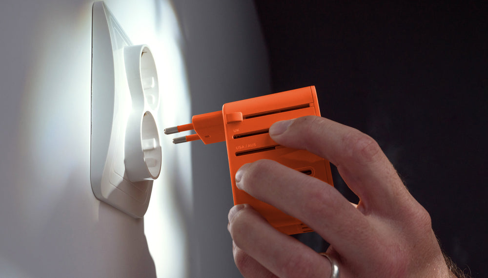 Hand placing orange travel adapter into European wall outlet