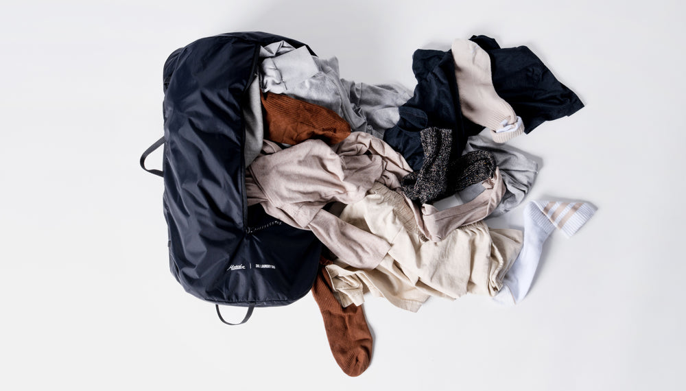 Laundry bag laying on white background with dirty laundry spilling out of the large side zipper