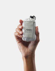 Hand holding a small white bag with a brand logo on a light gray background