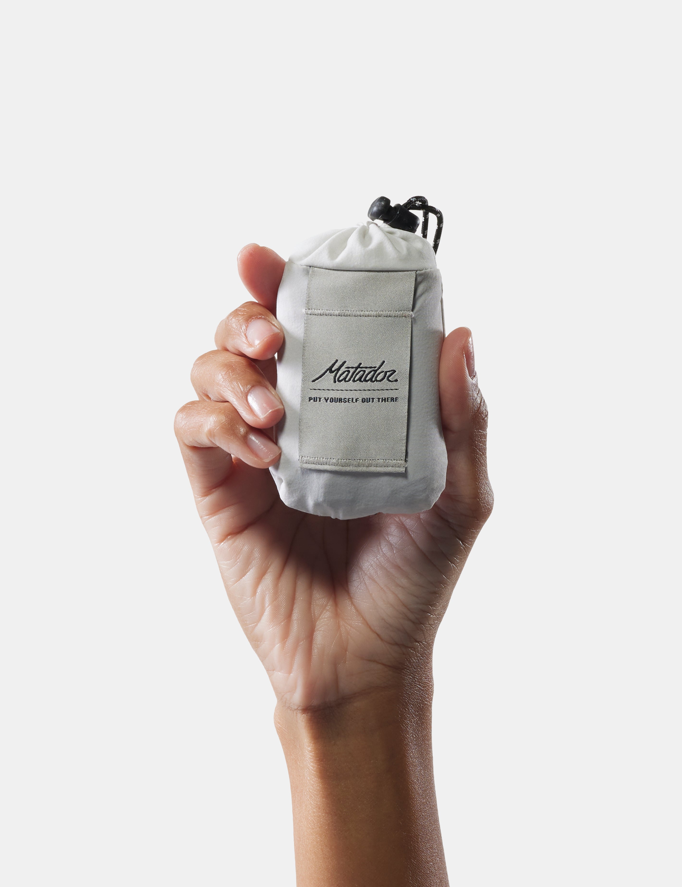 Hand holding a small white bag with a brand logo on a light gray background