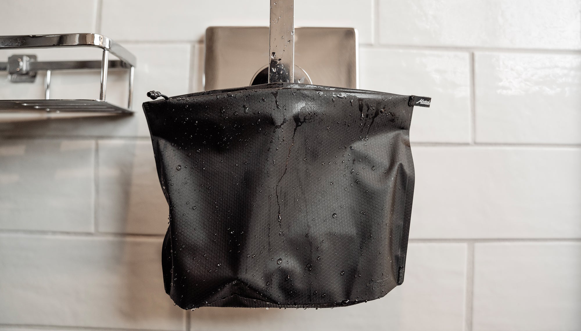 FlatPack Zipper Toiletry Case hanging from shower hook, beading with water