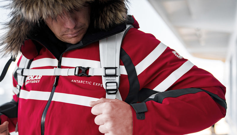 front view of man in red antarctic expedition jacket, pulling down shoulder straps of white SEG28