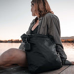 Woman sitting on lake dock with NanoDry Trek Towel case hanging from her black bag