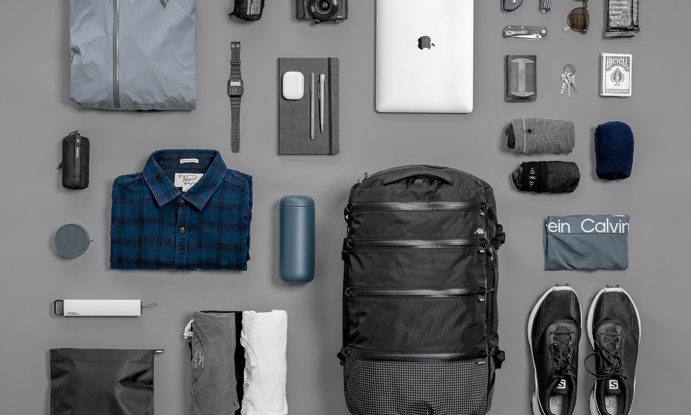 SEG28 laid flat on gray background with contents like clothing, laptop, sunglasses, snacks, and toiletries