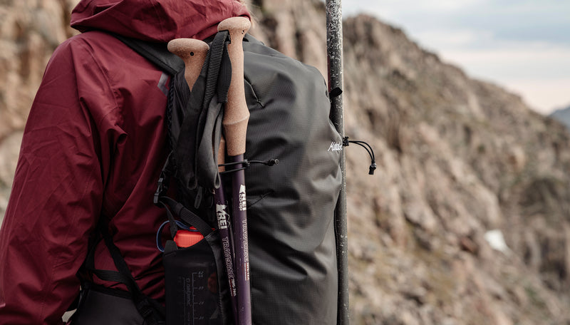 Woman in maroon jacket with trekking poles attached to her beast18 pack