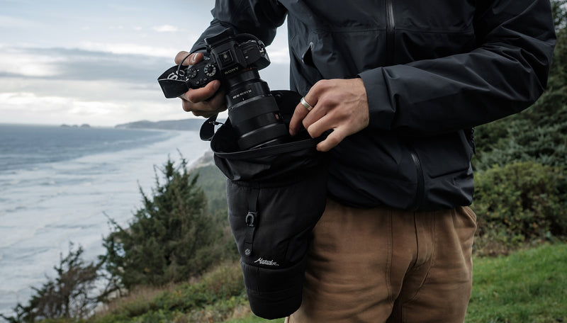 Man on shoreline, pulling camera out of camera base layer