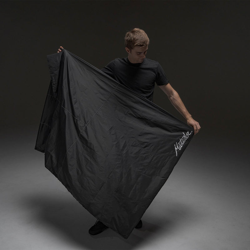 Man on dark gray background, holding fully open Pocket Blanket