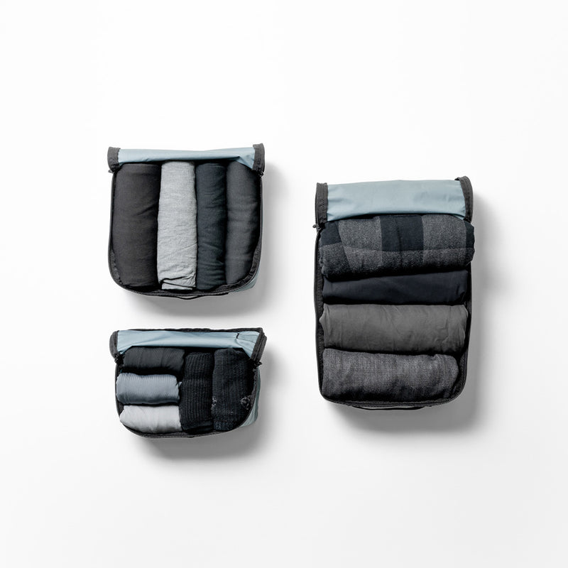 top view of 3 different sized packing cubes on white background. Each cube filled with monochromatic gray clothing