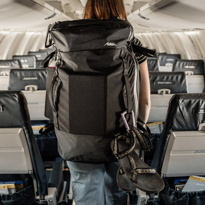 woman walking down airplane aisle with shoes handing off bag by carabiner