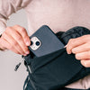 close up view of cell phone being placed in black sling bag