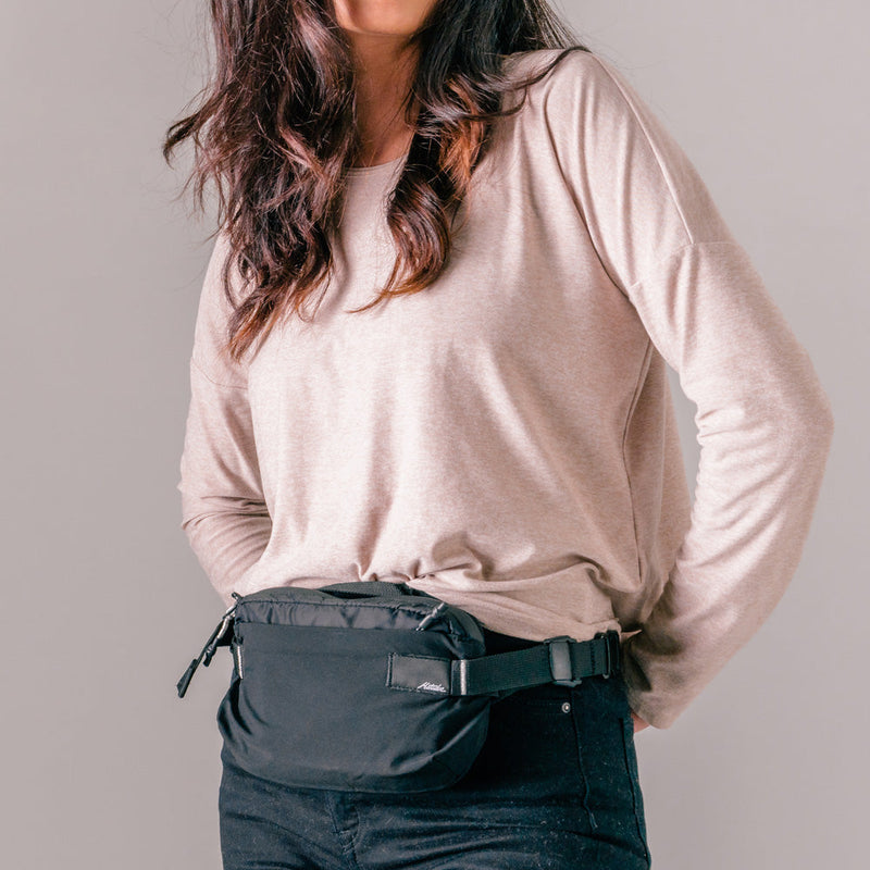 woman on light gray background wearing black sling bag across her front waist