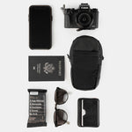 Collage of items laid out on white background: speedstash, phone, camera, passport, RXBar snack, sunglasses, wallet