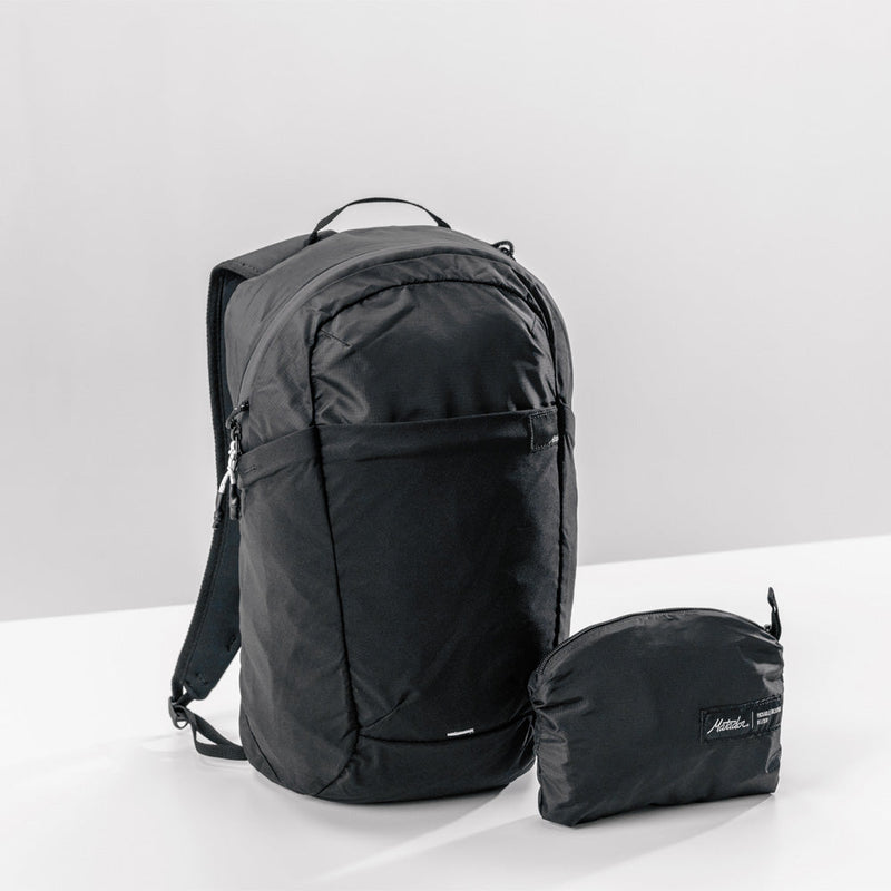 3/4 view of black backpack and packed up pouch on light gray background