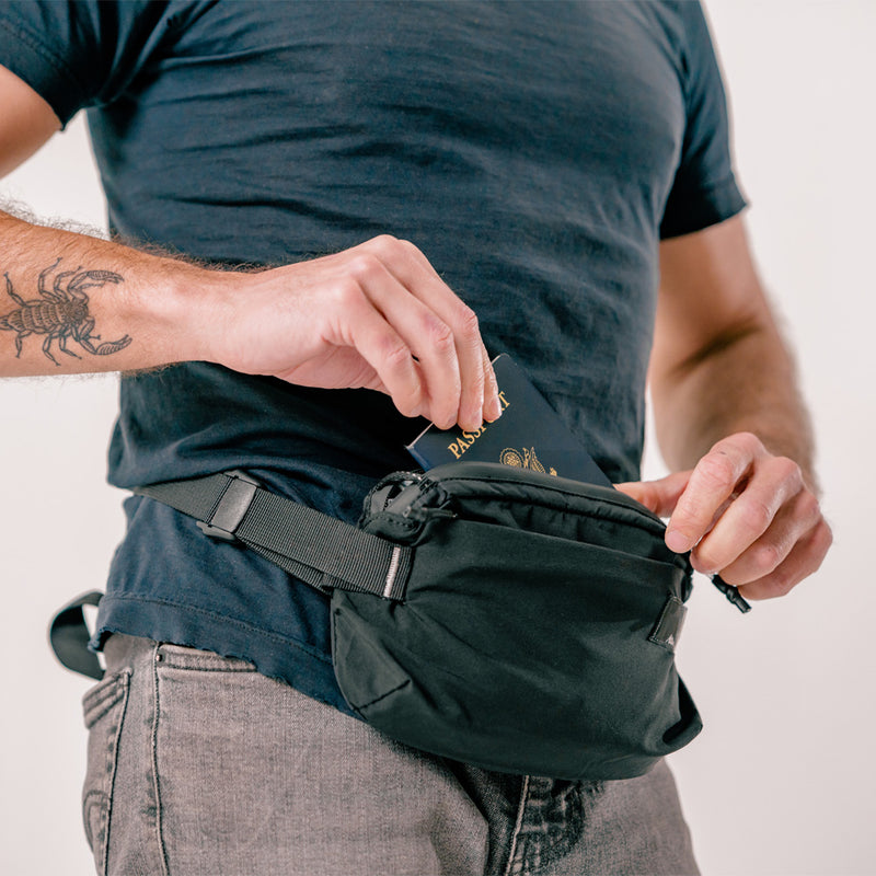 man placing passport into black sling back strapped to his front waist