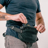 man placing passport into black sling back strapped to his front waist