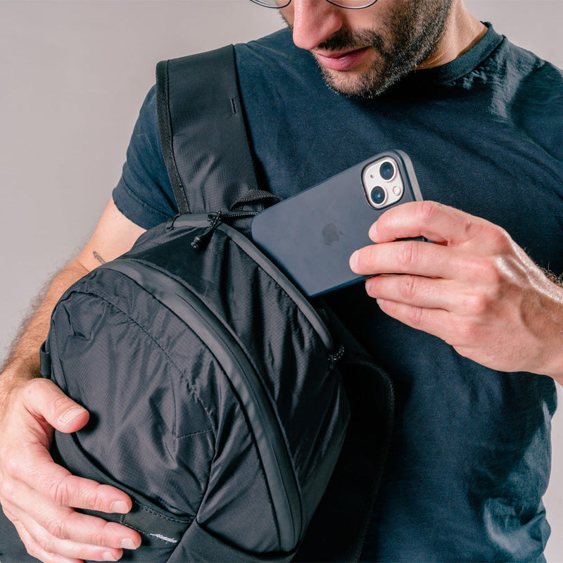 man putting cell phone into top zipper pocket of black backpack