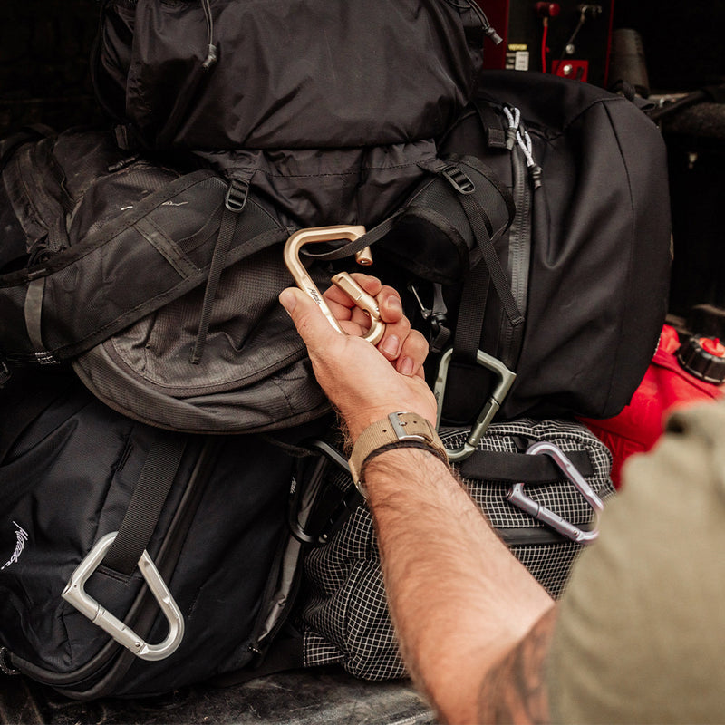 Hand unclipping gold carabiner from pile of bags