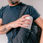 man putting water bottle into water bottle pocket of black backpack