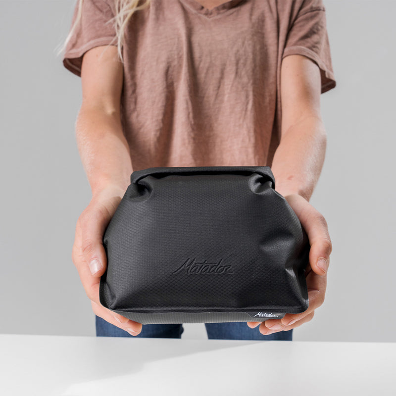 hands holding closed charcoal toiletry case straight to camera