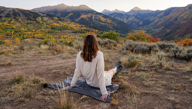 Woman sitting on Pocket Blanket Mini, looking out at autumn sunset over the mountains
