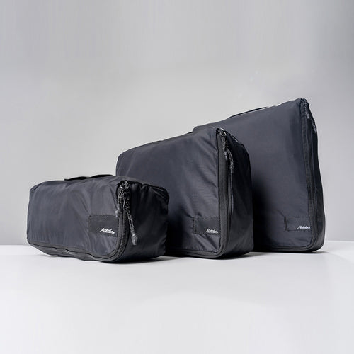 black small, medium and large packing cubes stacked next to each other on gray background