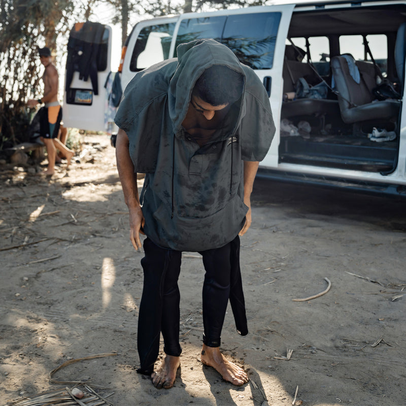 Man next to van at beach, changing out of wet suit while wearing poncho