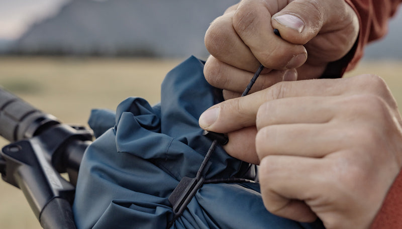 Close up view of man cinching down blue jacket to bike handlebars with ReTie