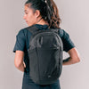 back view of woman wearing black backpack on light gray background