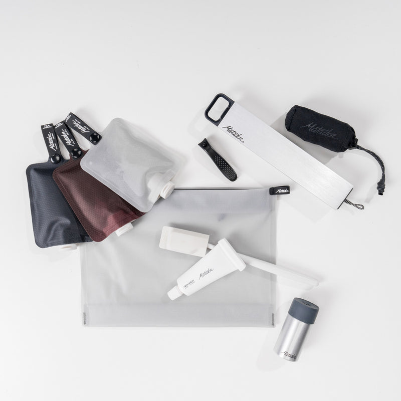 white backgroune with matador products laid out: toiletry bottles, pill canister, towel, waterproof canister, toothbrush cap, toothpaste tube and white zipper toiletry case