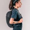 side view of woman wearing black backpack on light gray background