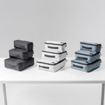 White table on light gray background with 3 packing cube sets in black, white, and slate