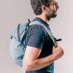 side view of man wearing slate blue backpack on light gray background