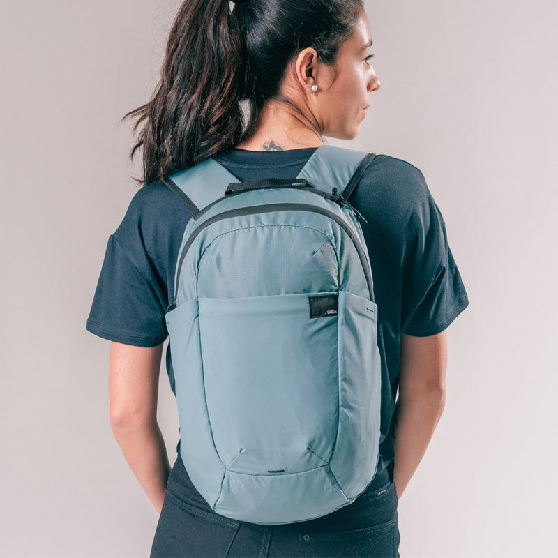 back view of woman wearing slate blue backpack on light gray background