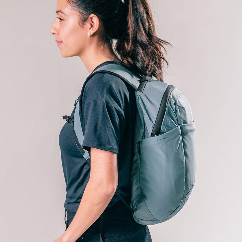 side view of woman wearing slate blue backpack on light gray background