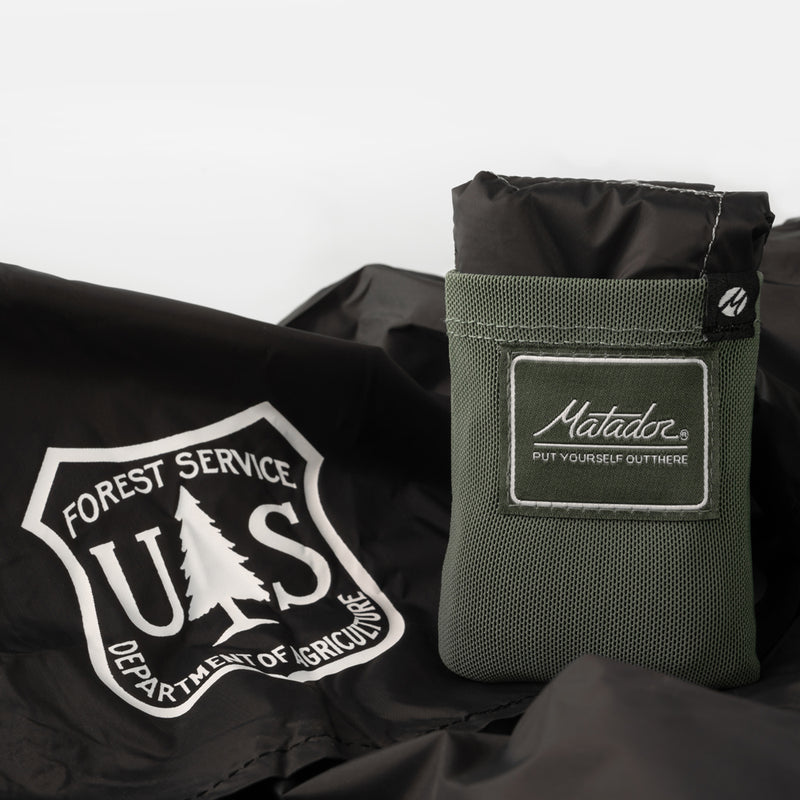 Packed up Green Pocket Blanket on an unfolded Pocket Blanket with US Forest Service logo
