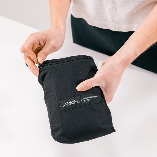 hands over white table, unzipping black duffle packable pocket