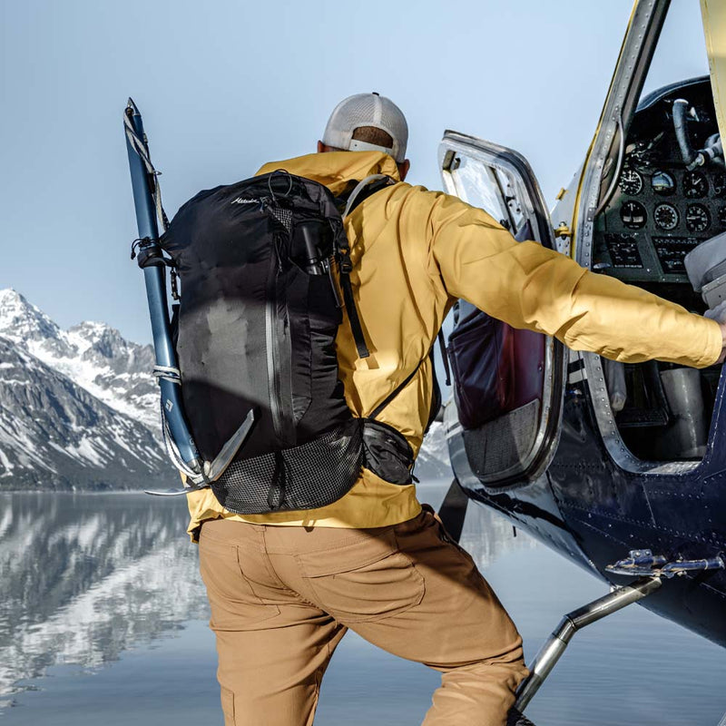 Back view of man wearing backpack and yellow jacket getting into sea plane in front of alaskan mountain scape 
