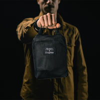 man in black studio holding out packed up backpack