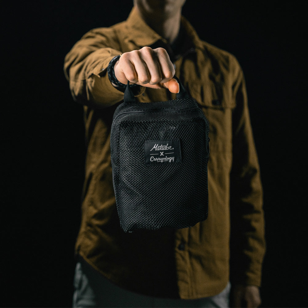 man in black studio holding out packed up messenger bag