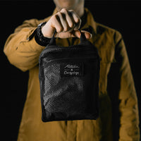 man on black studio background holding packed up white backpack in mesh bag