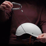 person in dark maroon shirt, holding white helmet with accessory cable running through it attached to a silver betalock