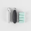 White and black silicone earplug cases + 4 mint colored ear plugs laying on light gray background