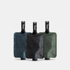 3 multi colored FlatPak Toiletry Bottles—charcoal, slate blue, and sage—on light gray background